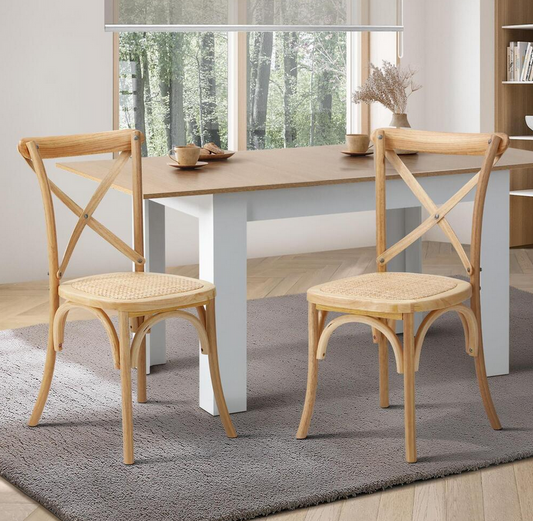 Two wooden Kross chairs with wicker seats in front of a dining table with a window view.